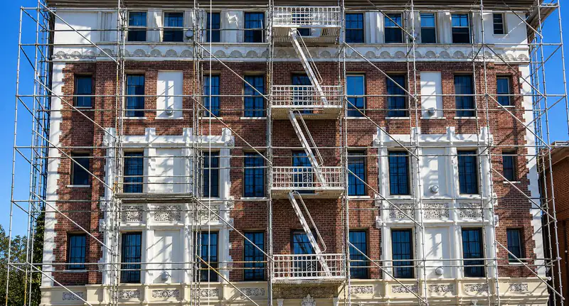 Frame scaffold on every floor of an ornate red brick building with white trim and iron fire escapes