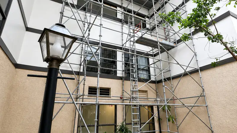 Scaffold wrapping a multi-story building with a lamp post and landscaping in the foreground