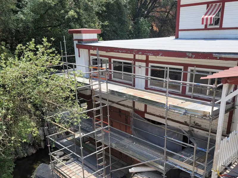 Scaffold with guardrails along the side of a two-story building surrounded by trees
