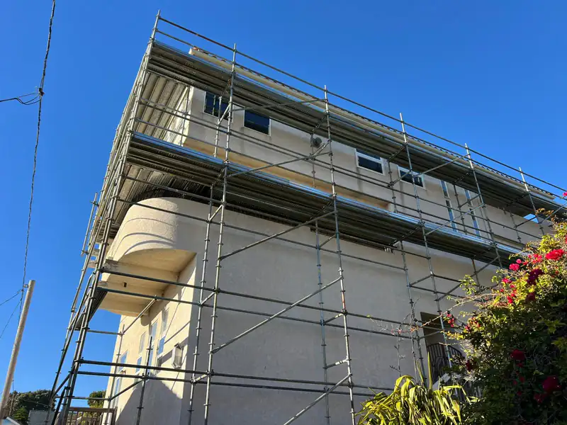 Scaffold with plank decks along the upper floors of a cream-colored building with a curved corner