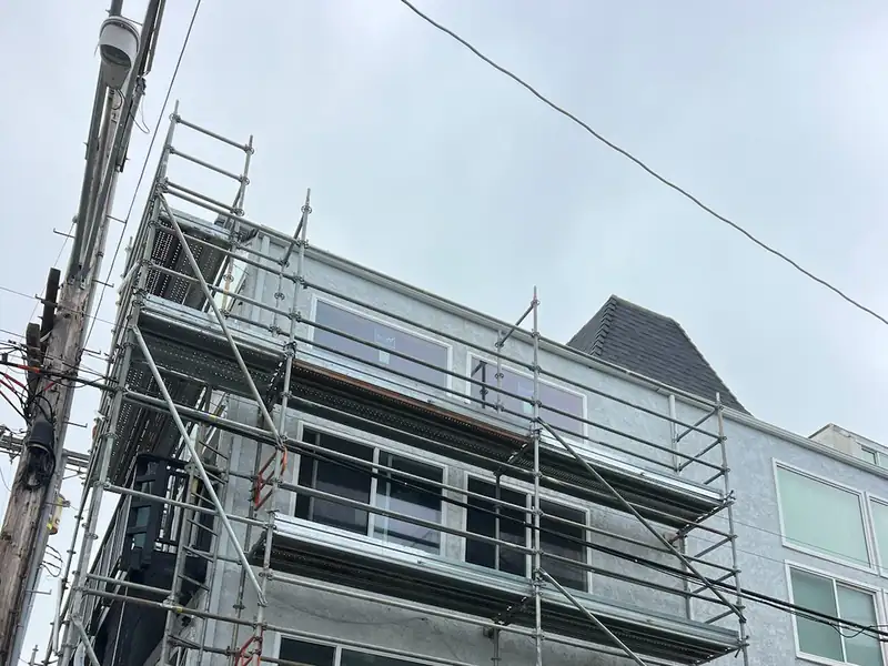 Frame scaffold with guardrails on every level running up the face of a four-story stucco building